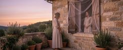 Illustration réaliste et sobre d’une femme en vêtements longs et clairs sur la terrasse d’une maison provençale au crépuscule, avec une moustiquaire visible à la fenêtre.